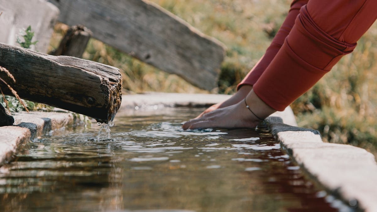 Hands in a tranquil mountain spring fountain in Trentino-South Tyrol, Italy, showcasing summer refreshment.